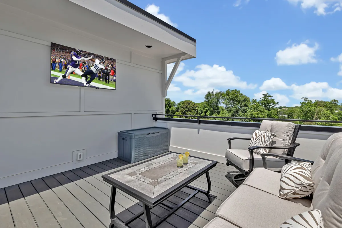 A stylish private rooftop patio featuring outdoor seating, a television, and views of greenery, set for relaxing or entertaining guests under the night sky.