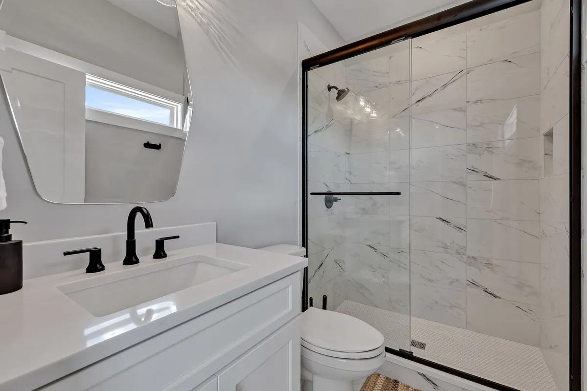 A modern bathroom with a large vanity, sleek sink, expansive mirror, and a glass shower enclosure. The space is bright and fresh, creating a spa-like environment ideal for self-care and relaxation.