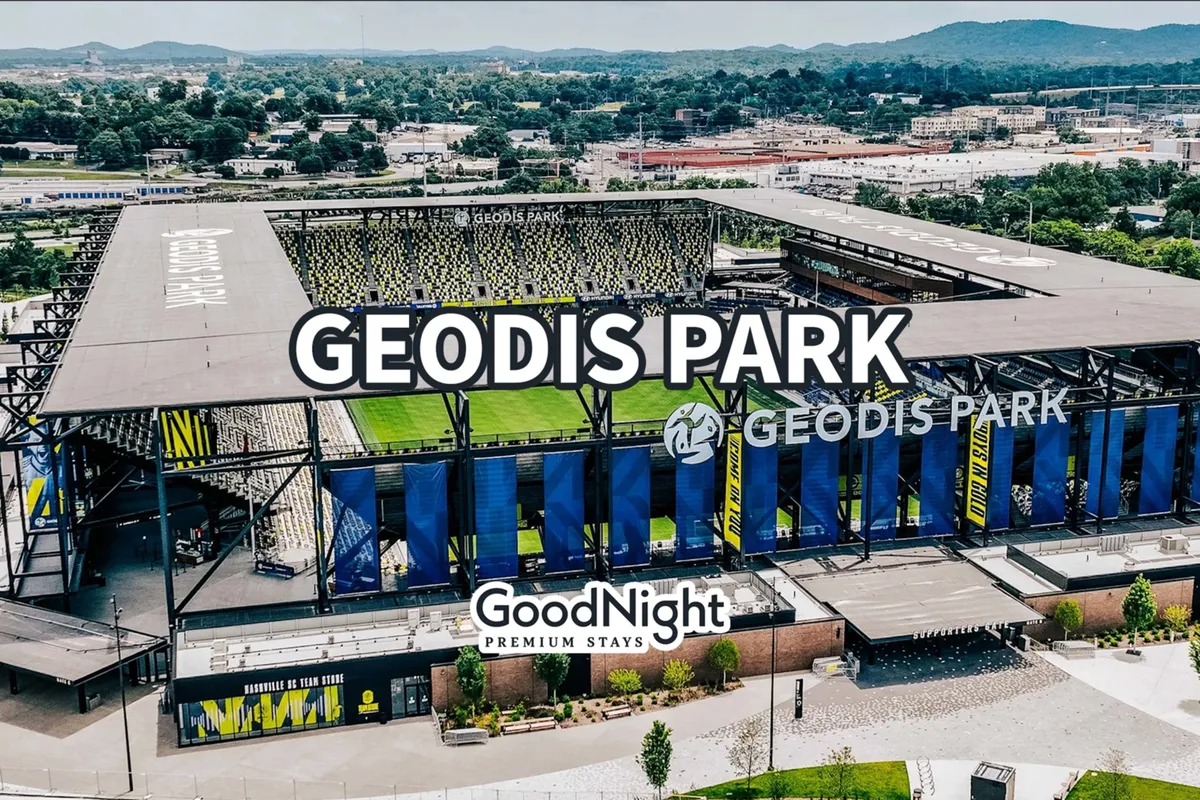 Geodis Park stadium is visible with its distinctive architecture, the GoodNight Premium Stays logo, and lush greenery and mountains in the background. The scene is lively, hinting at sports, concerts, and community gatherings.