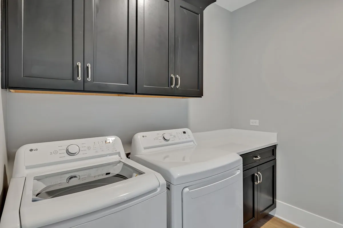 A bright, well-organized laundry area featuring a modern washing machine and dryer set beneath white cabinets. The space is clean, tidy, and fully equipped, suggesting ease of use and practicality, with storage for laundry supplies above.