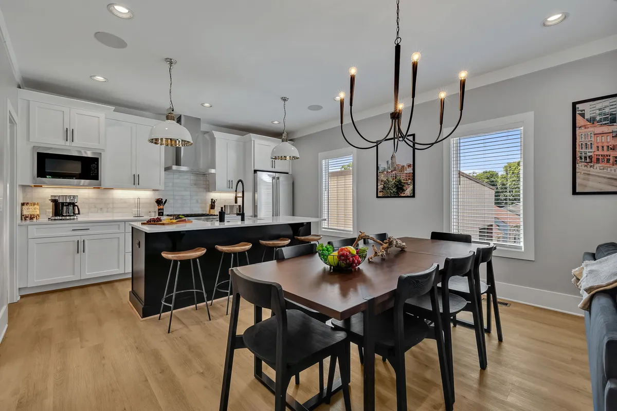 A combined kitchen and dining space featuring a kitchen island, an elegant dining table that seats eight, a statement chandelier, and engaging wall art. The layout is open and inviting, designed for easy movement between cooking, dining, and entertaining.