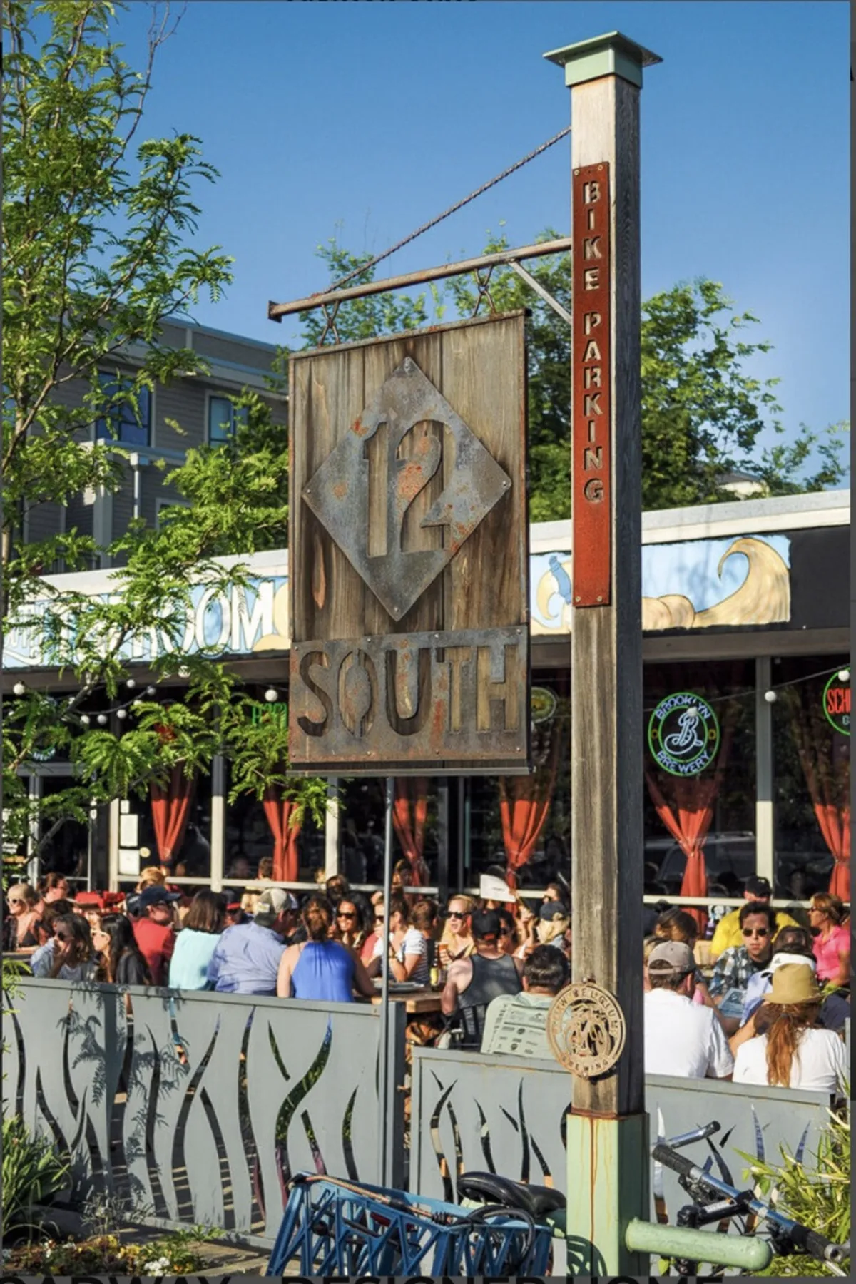 A lively street scene featuring the '12 SOUTH' sign, bustling outdoor seating, and a bike parking sign. The setting is vibrant and social, ideal for dining, people-watching, and experiencing local culture.